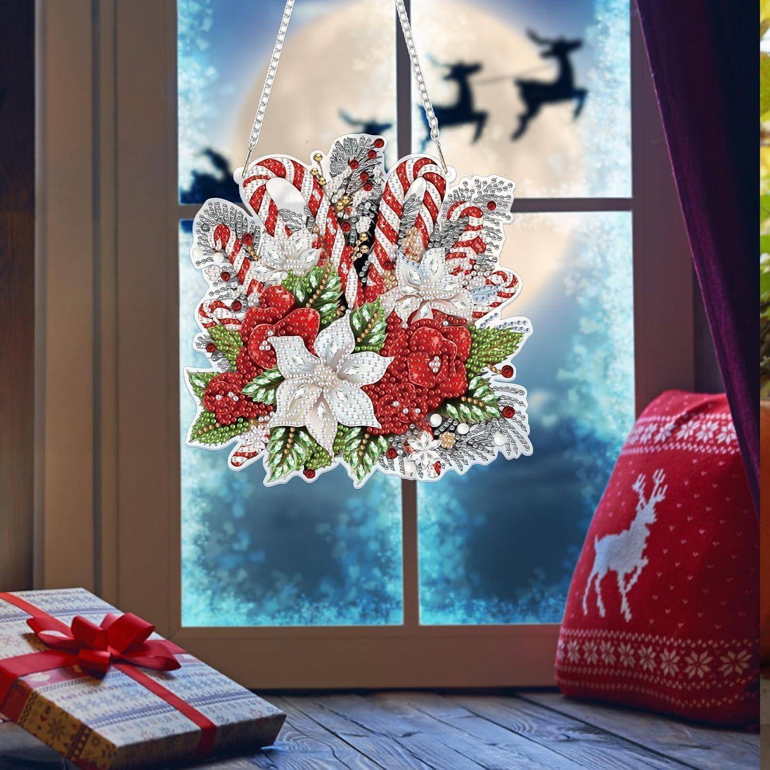 Ein festliches Weihnachtsornament mit Zuckerstangen, weißen Blüten und roten Beeren hängt in einem Fenster, in der Nähe liegen ein eingepacktes Geschenk und ein roter Rentier-Pullover.