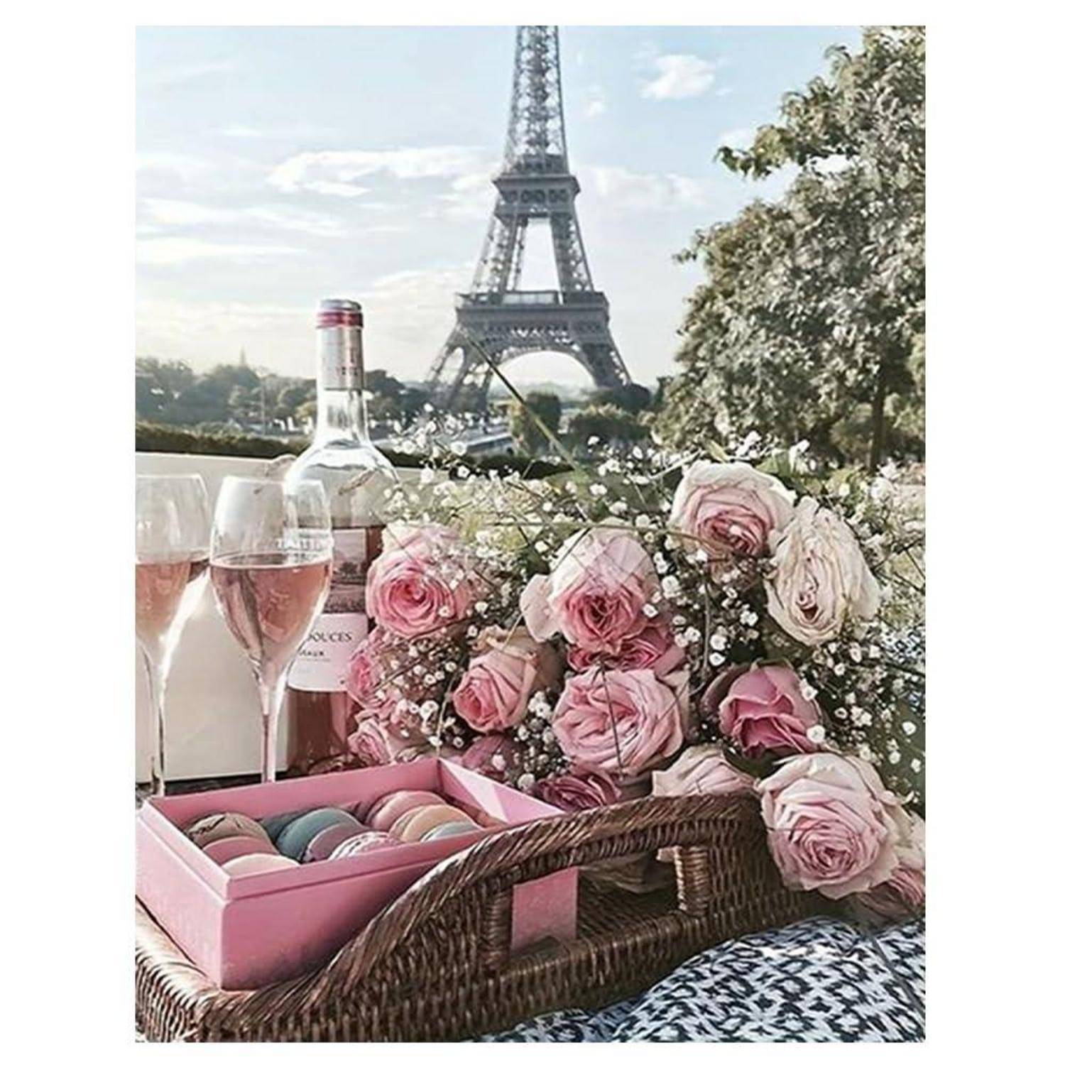 Romantisches Picknick-Setup mit rosa Rosen, Macarons, Weingläsern und einer Flasche vor dem Eiffelturm in Paris.
