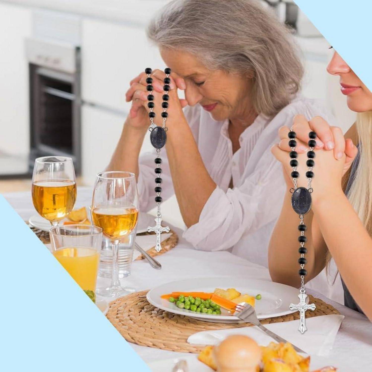 Zwei Frauen an einem Tisch beten mit Rosenkranzperlen vor einer Mahlzeit, mit Gläsern und Tellern, die zum Essen gedeckt sind.
