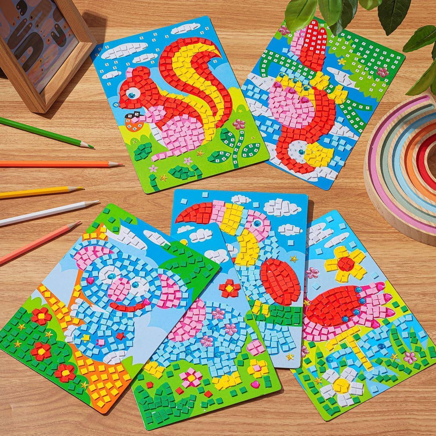Mehrere bunte Mosaikkunstkarten mit Tieren aus Vögeln und einer Schlange liegen auf einem Holztisch mit farbigen Bleistiften und einer Malpalette in der Nähe.