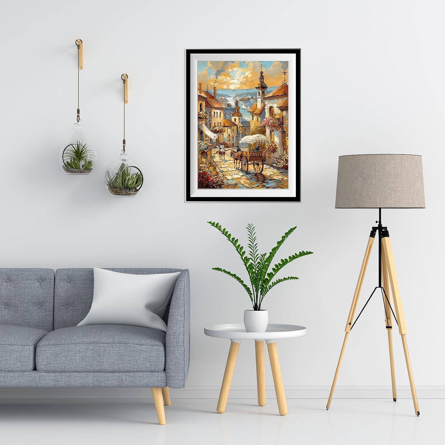Modernes Wohnzimmer mit grauem Sofa, gerahmtem Kunstwerk, hängenden Pflanzen, kleinem Tisch mit Topfpflanze und Stehleuchte auf Dreibein.