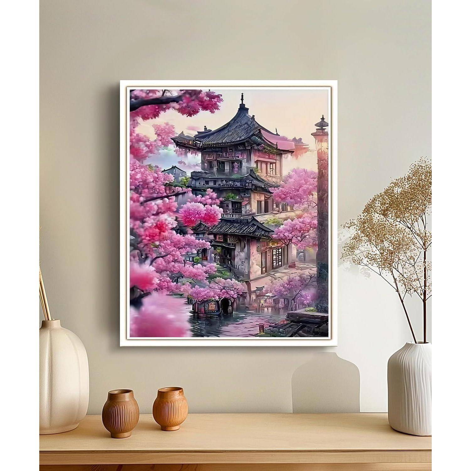 Gerahmtes Gemälde eines traditionellen mehrstöckigen asiatischen Tempels neben rosa Kirschblüten, ausgestellt auf einem minimalistischen Regal in einem Zimmer.