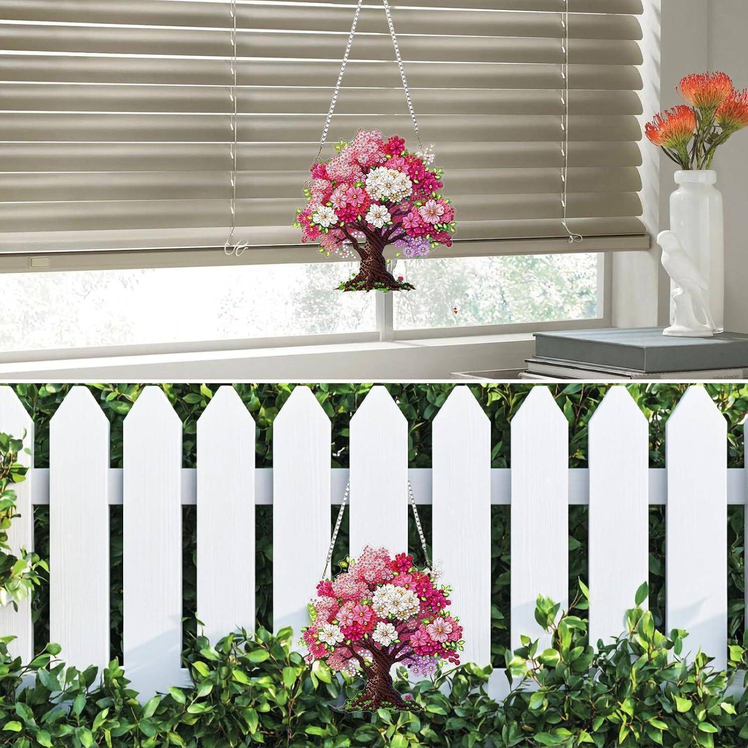 Dekorative rosa blühende Baum-Ornamente, die im Innenbereich hängend und an einem weißen Lattenzaun im Freien gezeigt werden, was Möglichkeiten zur Wohnungsausstattung suggeriert.