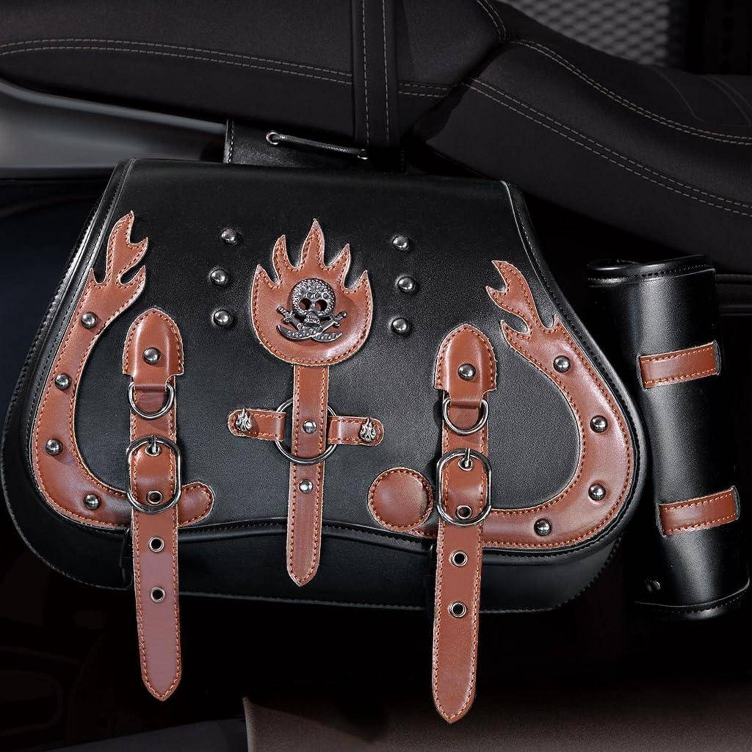 Schwarze Ledertasche im Sattelstil mit braunen Flammen- und Totenkopf-Riemenakzenten und Metallnieten, vor dunklem Hintergrund gezeigt.