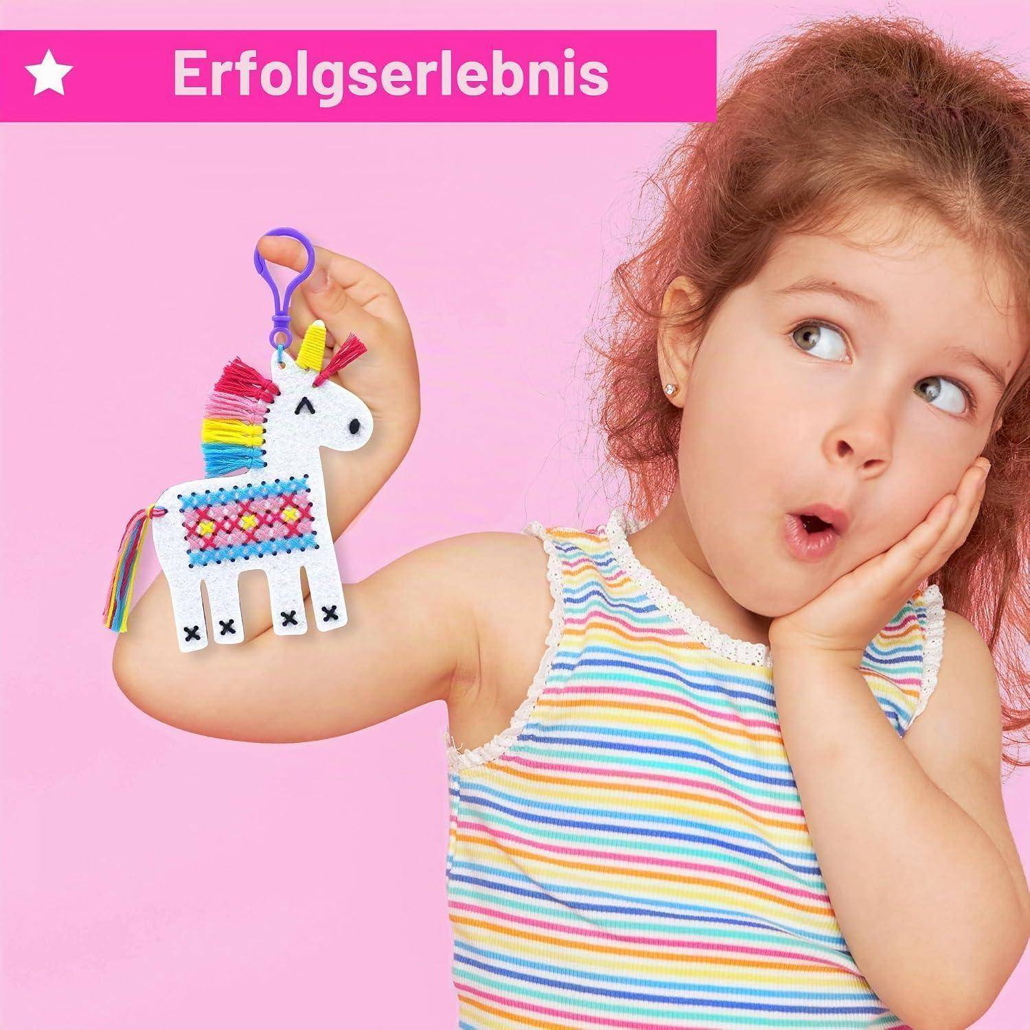 Junges Mädchen posiert vor einem rosa Hintergrund und hält ein farbenfrohes selbstgebasteltes Einhorn-Kunstwerk, mit dem Wort „Erfolgserlebnis