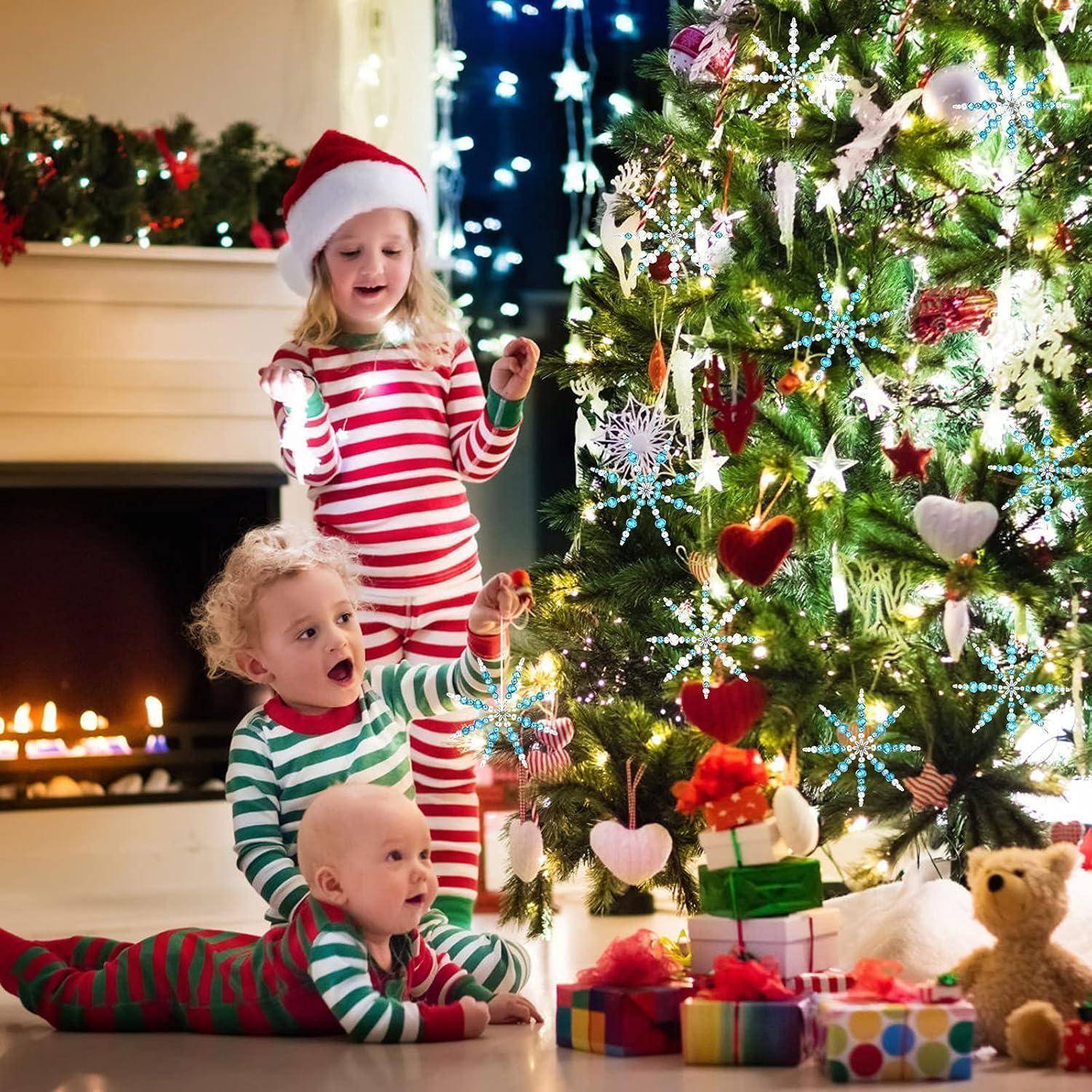 Drei Kinder in gestreiften Pyjamas schmücken einen leuchtenden Weihnachtsbaum neben eingepackten Geschenken und einem Kamin.