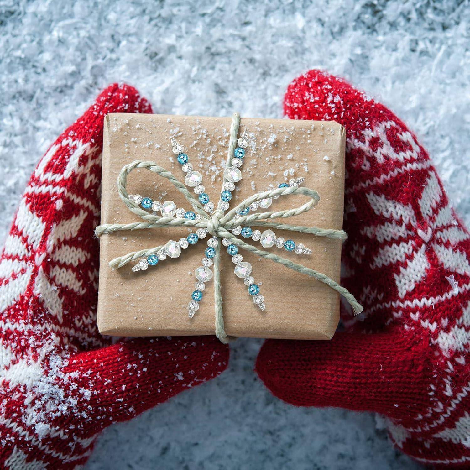 Rote Strickhandschuhe halten eine kleine, mit Schnur gebundene Geschenkschachtel mit einer Perlenschneeflocke, bestäubt mit Schnee.