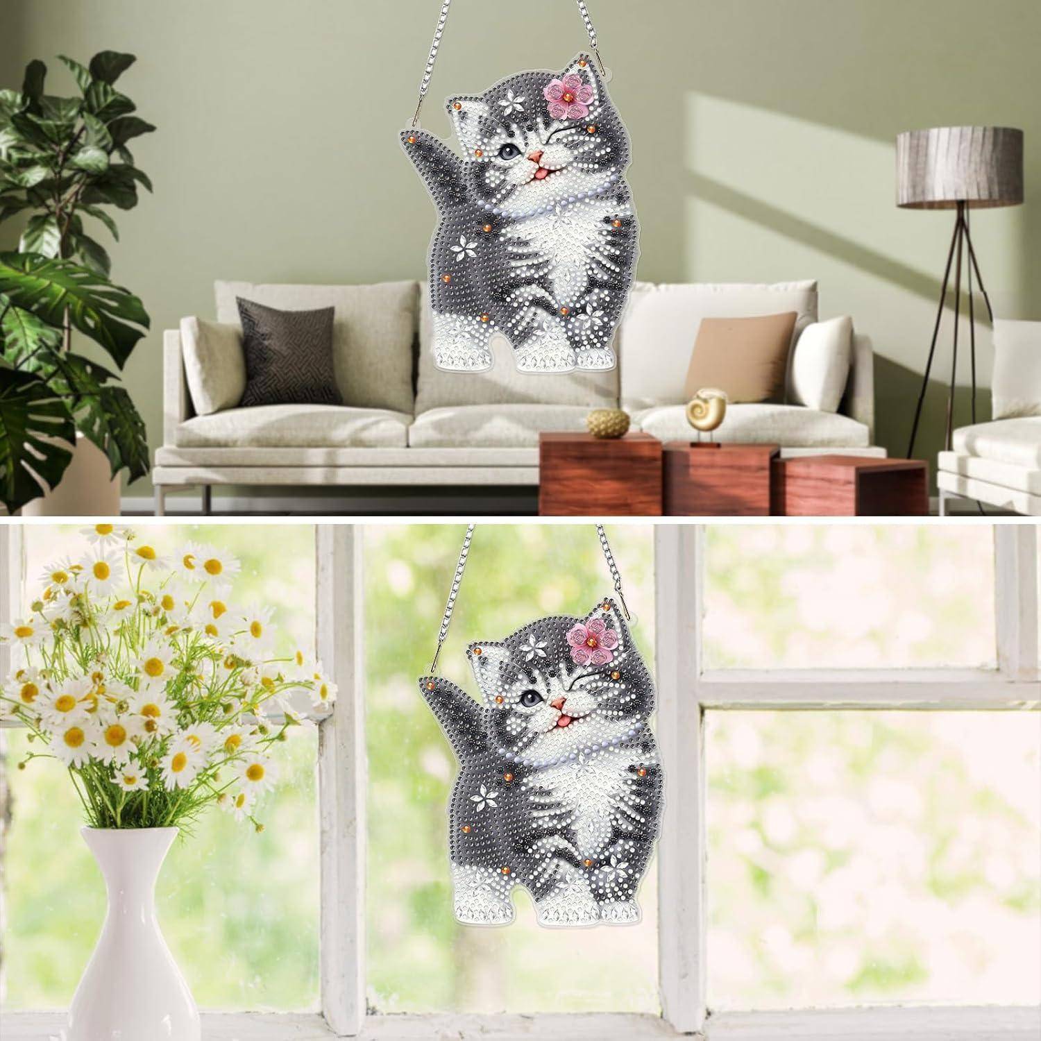Funkelnde katzenförmige Hängdekoration mit einer rosa Blume, die drinnen im Wohnzimmer und an einem Fenster neben Blumen angezeigt wird.