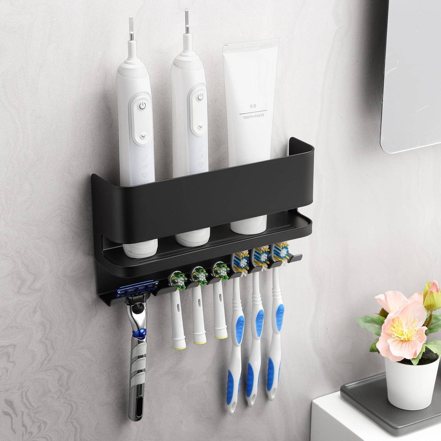 An der Wand angebrachter Badezimmerorganizer, der zwei elektrische Zahnbürsten, eine Zahnpastatube und mehrere manuelle Zahnbürsten hält, mit einem darunter befestigten Rasierer.