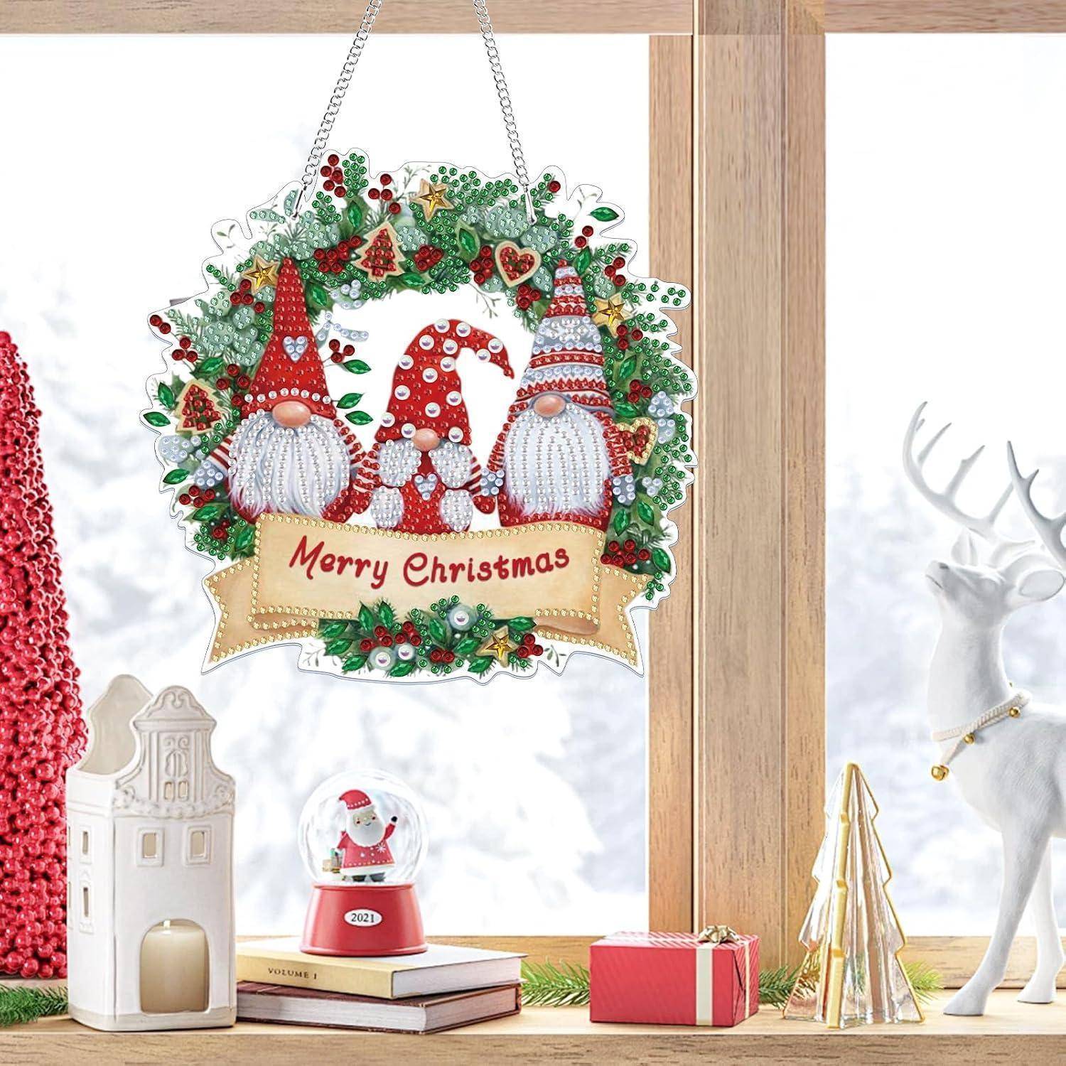 Weihnachtszwerg-Kranzmament mit 'Frohe Weihnachten'-Text, hängend in einer festlichen Fensterausstellung mit Büchern, Geschenkbox, Kerzenhalter und Rentierdeko.
