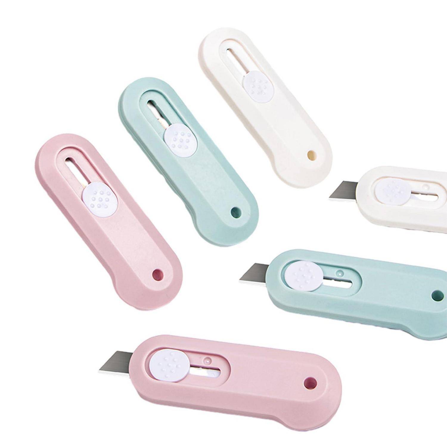Fünf pastellfarbene Universalmesser in Rosa, Mintgrün und Weiß, jeweils mit einer verschieblichen Klinge und einem runden Sicherheitsverriegelungsknopf auf weißem Hintergrund.