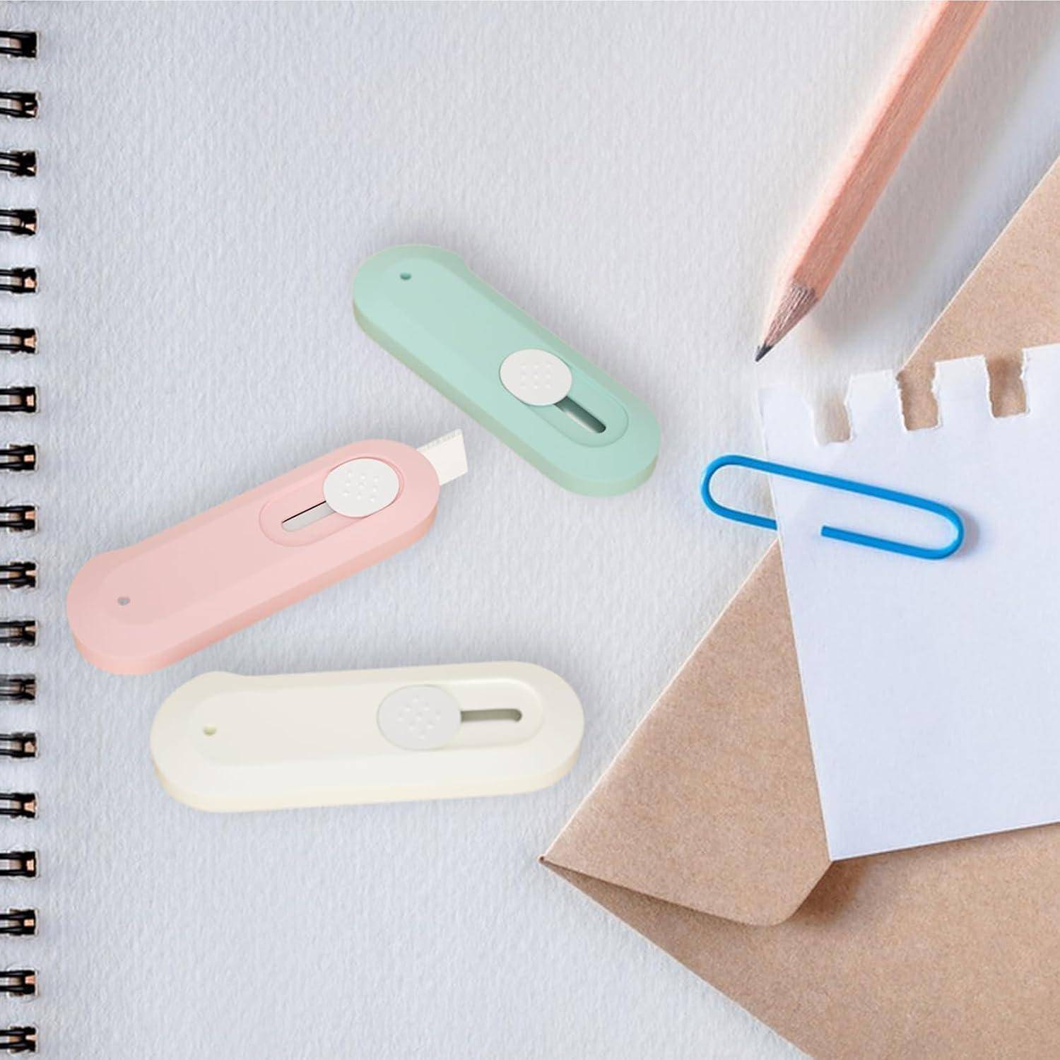 Pastellfarbene magnetische Kabelclips, eine blaue Büroklammer, ein Bleistift und ein Notizbuch auf einem Schreibtisch mit Blättern Papier und einem Kraftpapierumschlag.