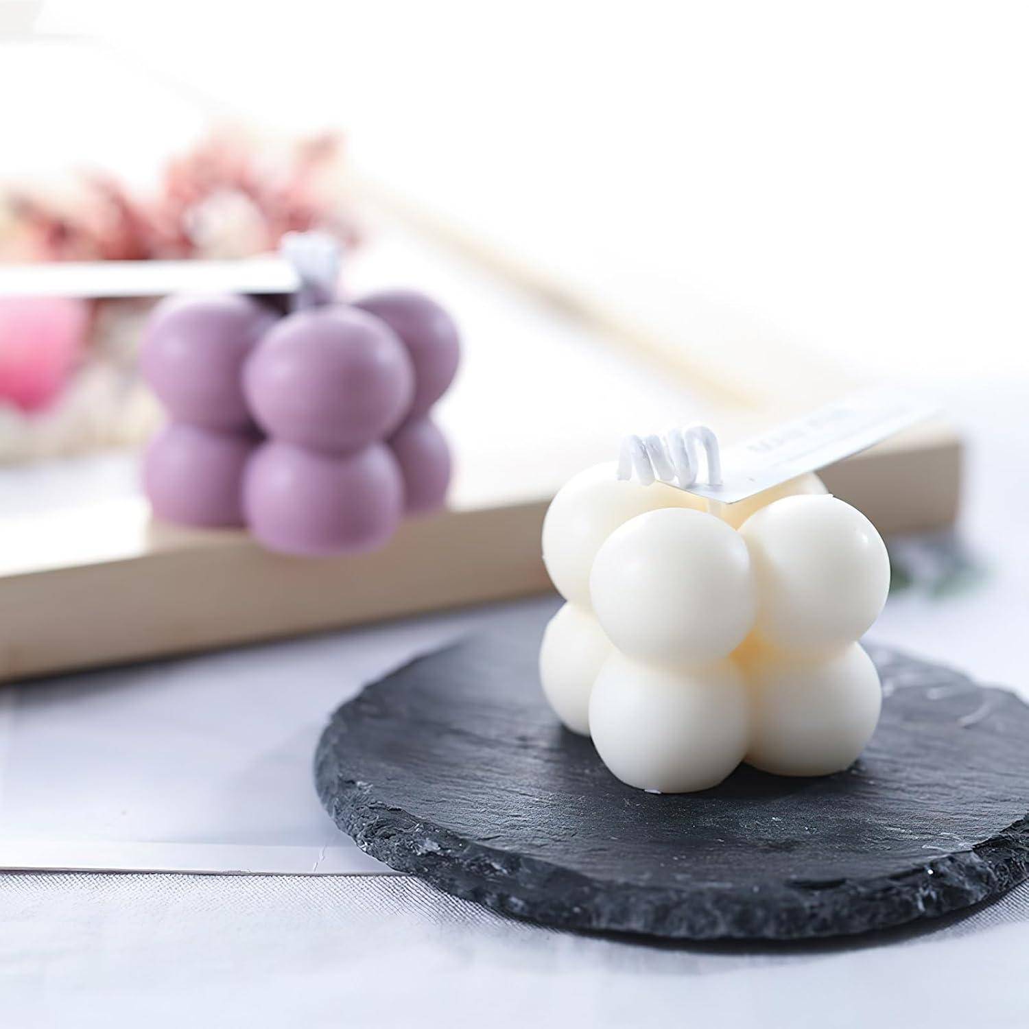 Weiße kugelförmige Dessert mit einem kleinen 'Mutter'-Topper auf einem schwarzen Schiefer-Untersetzer, mit einer unscharfen violetten Version im Hintergrund.