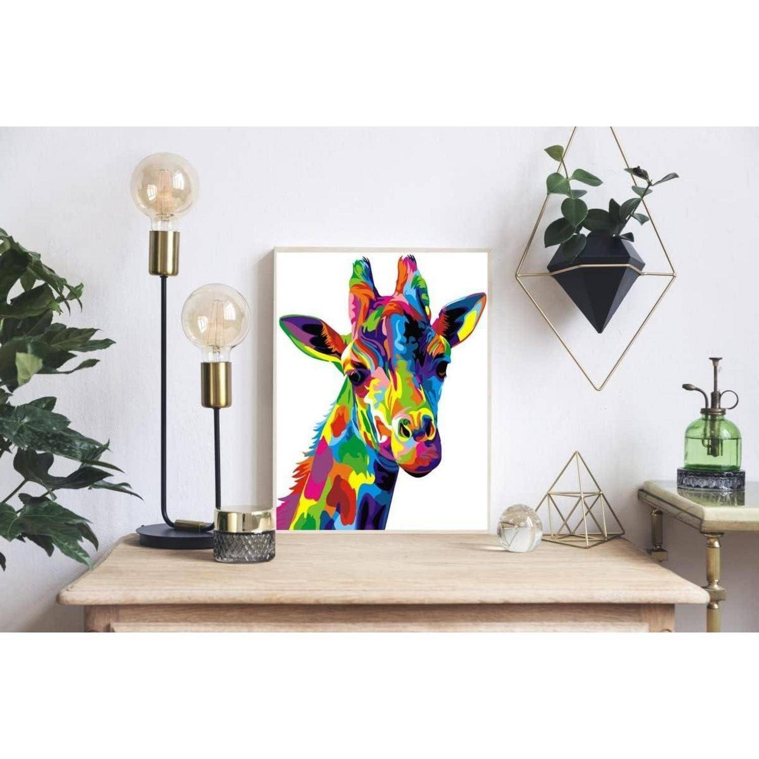 Farbenfroches Giraffenporträt-Druck auf einem Tisch in einem modern gestalteten Raum, umgeben von Lampen, Pflanzen und geometrischer Dekoration.