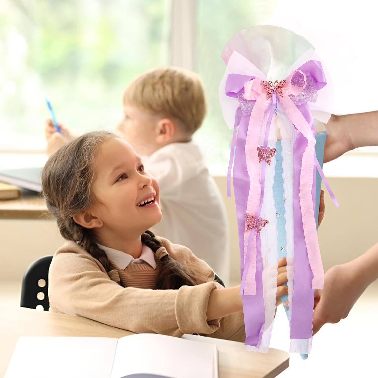 Lächelndes junges Mädchen im Klassenzimmer erhält einen Pastellfarbenen Bandstab von einem Erwachsenen, während ein anderes Kind im Hintergrund zeichnet.