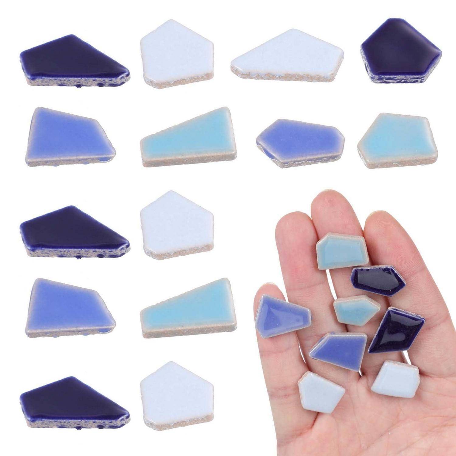 Kleine blaue, weiße und violette Mosaikglaskacheln auf weißem Hintergrund dargestellt, wobei mehrere Stücke in der Hand einer Person gehalten werden, um die Größe zu zeigen.