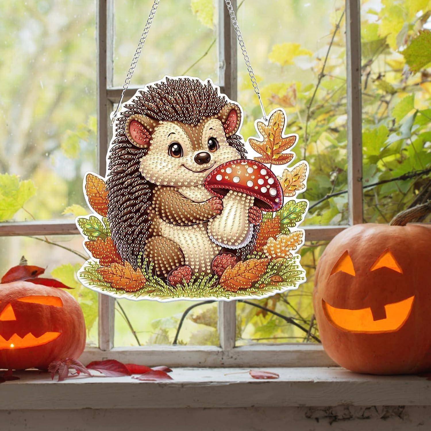 Herbstdekoration mit einem aufgehängten Igel, der einen Pilz hält, ausgestellt zwischen zwei geschnitzten Kürbislaternen auf einer Fensterbank.