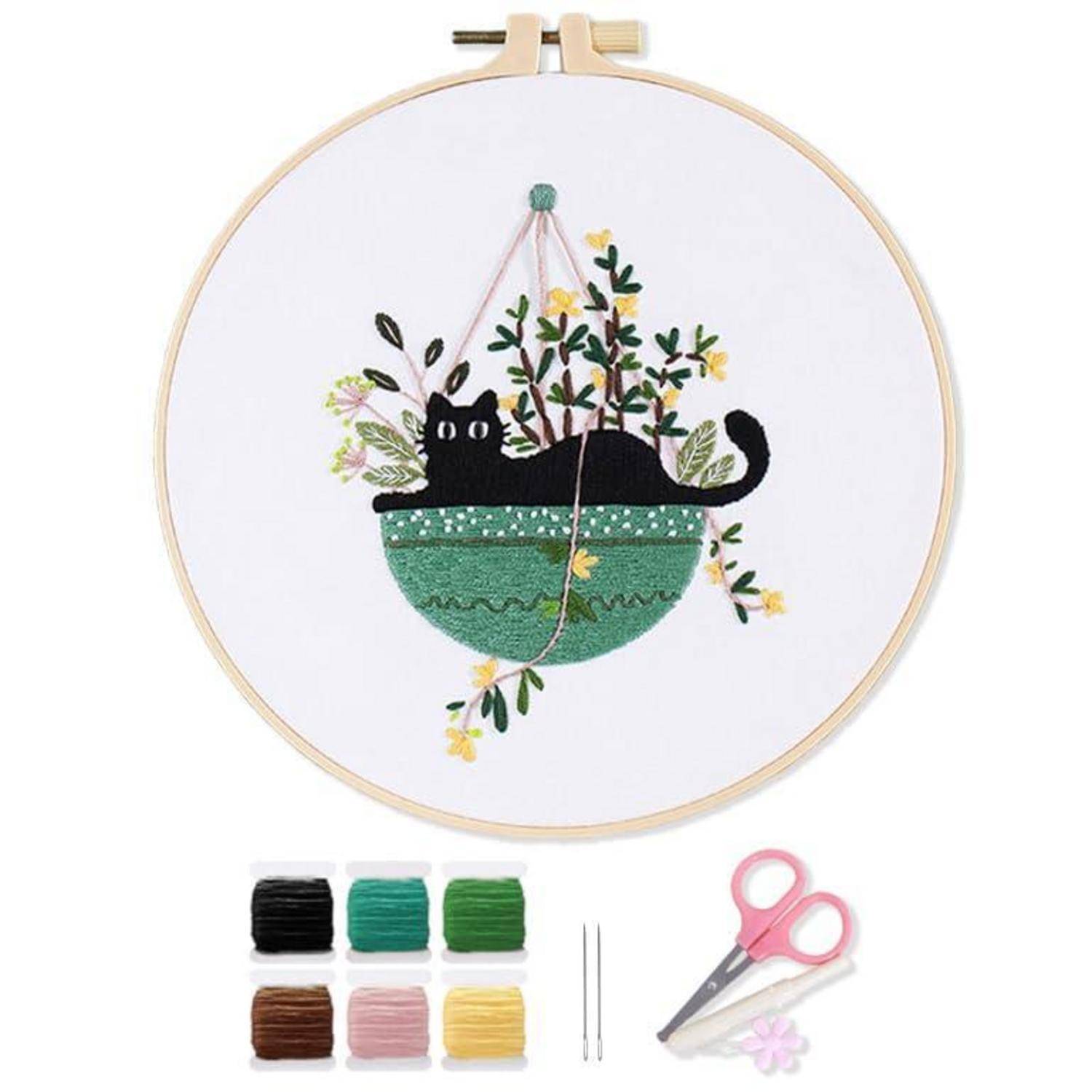 Stickrahmen-Bastelset mit einer schwarzen Katze in einem grünen hängenden Blumentopf mit Blumen, darunter Fäden, Nadeln und Schere.
