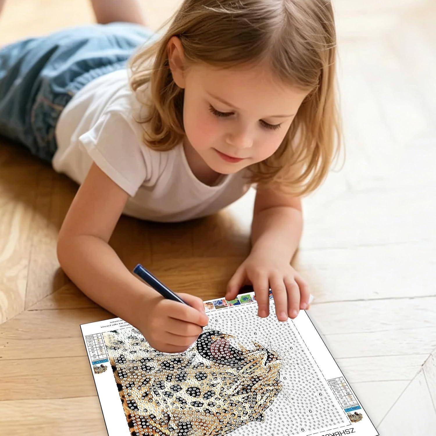 Junges Mädchen, das auf dem Boden liegt und sich konzentriert, während es einen Stift verwendet, um ein Diamond Painting oder Punkt-zu-Punkt-Kunstwerk auf einem Arbeitsblatt auszufüllen.