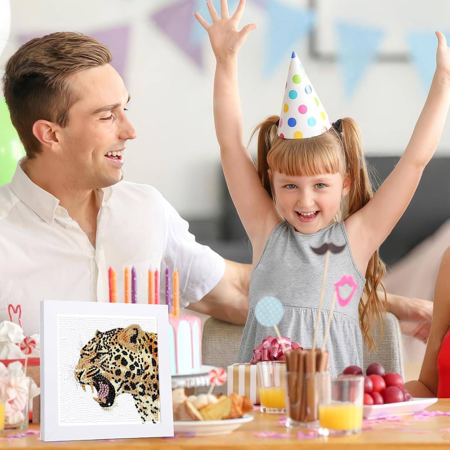Lächelndes Mädchen mit Partyhut hebt die Arme an einem Geburtstagstisch, mit einem Mann neben ihr und Kuchen, Kerzen und Snacks davor.