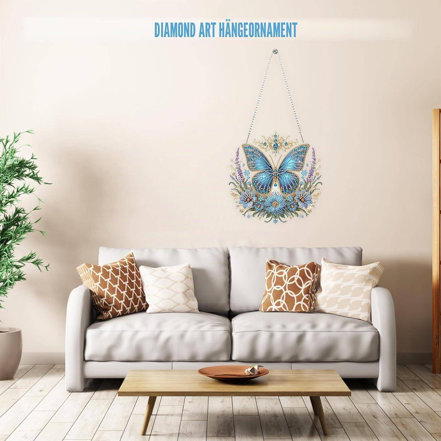 Wohnzimmer mit einem grauen Sofa unter einem Wandkunst-Hängornament mit blauem Schmetterlingsdesign und dem Text „DIAMOND ART HÄNGEORNAMENT