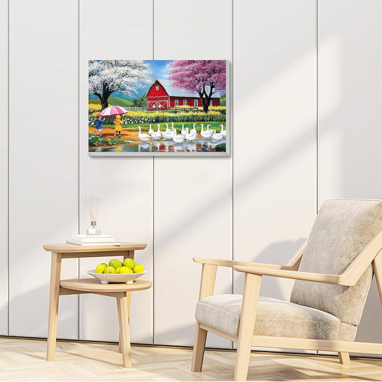 Ein hell gerahmtes Gemälde über einem beigen Sessel zeigt eine rote Scheune, blühende Bäume und Gänse an einem Teich in einem minimalistischen Wohnzimmer.