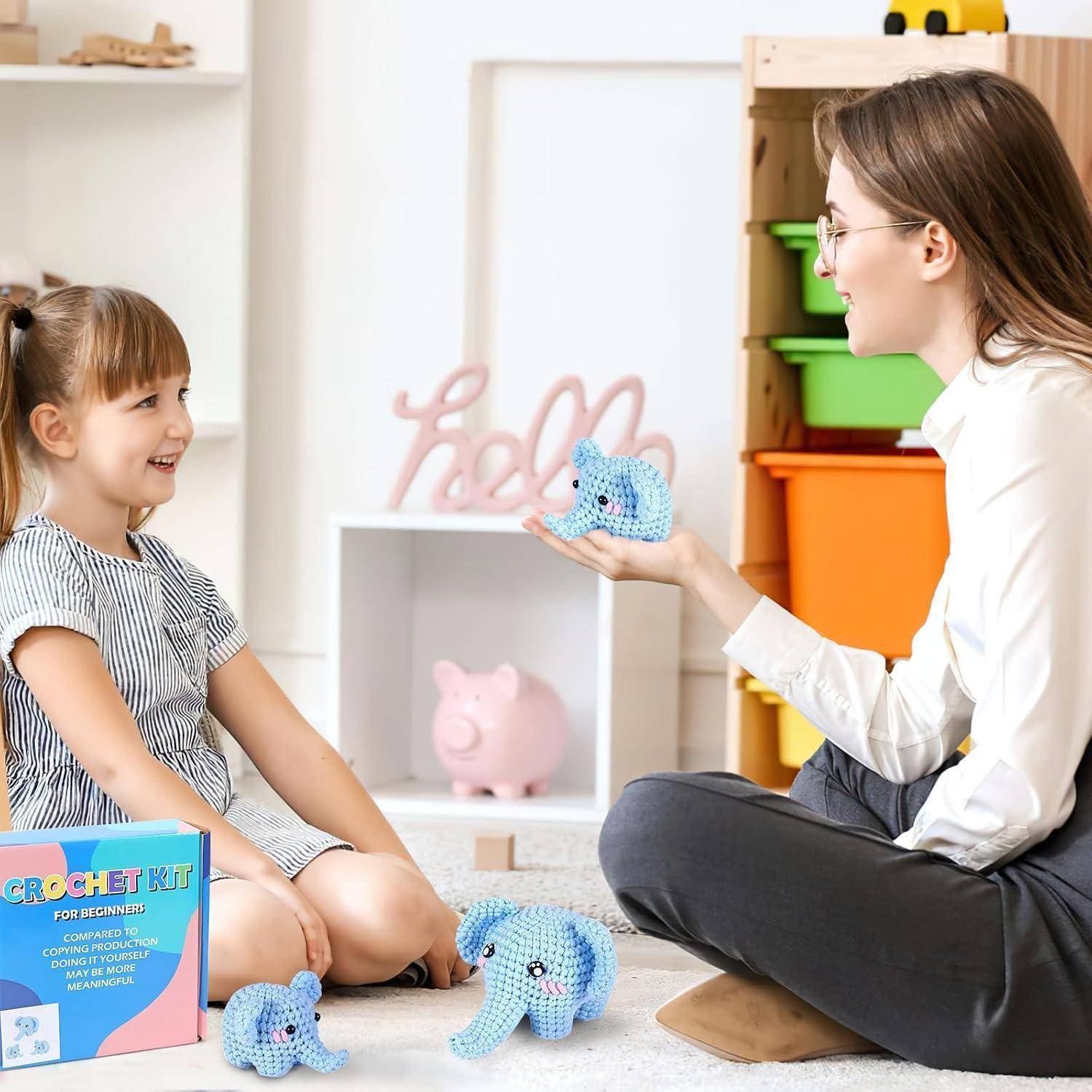 Frau unterrichtet ein lachendes Kind über gehäkelte Tierspielzeuge in einem Spielzimmer, mit Garntieres und einer sichtbaren Häkelset-Box.