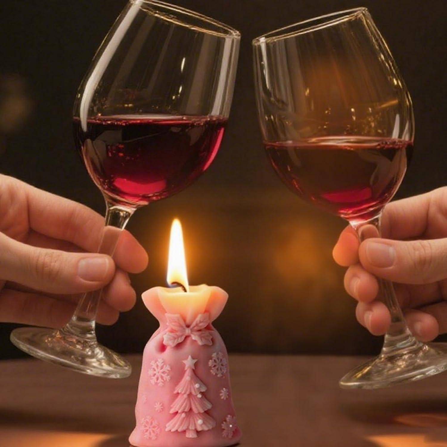Zwei Hände stoßen mit Rotweingläsern neben einer brennenden rosa Dekorationskerze auf einem Tisch an und schaffen eine warme Feierszene.
