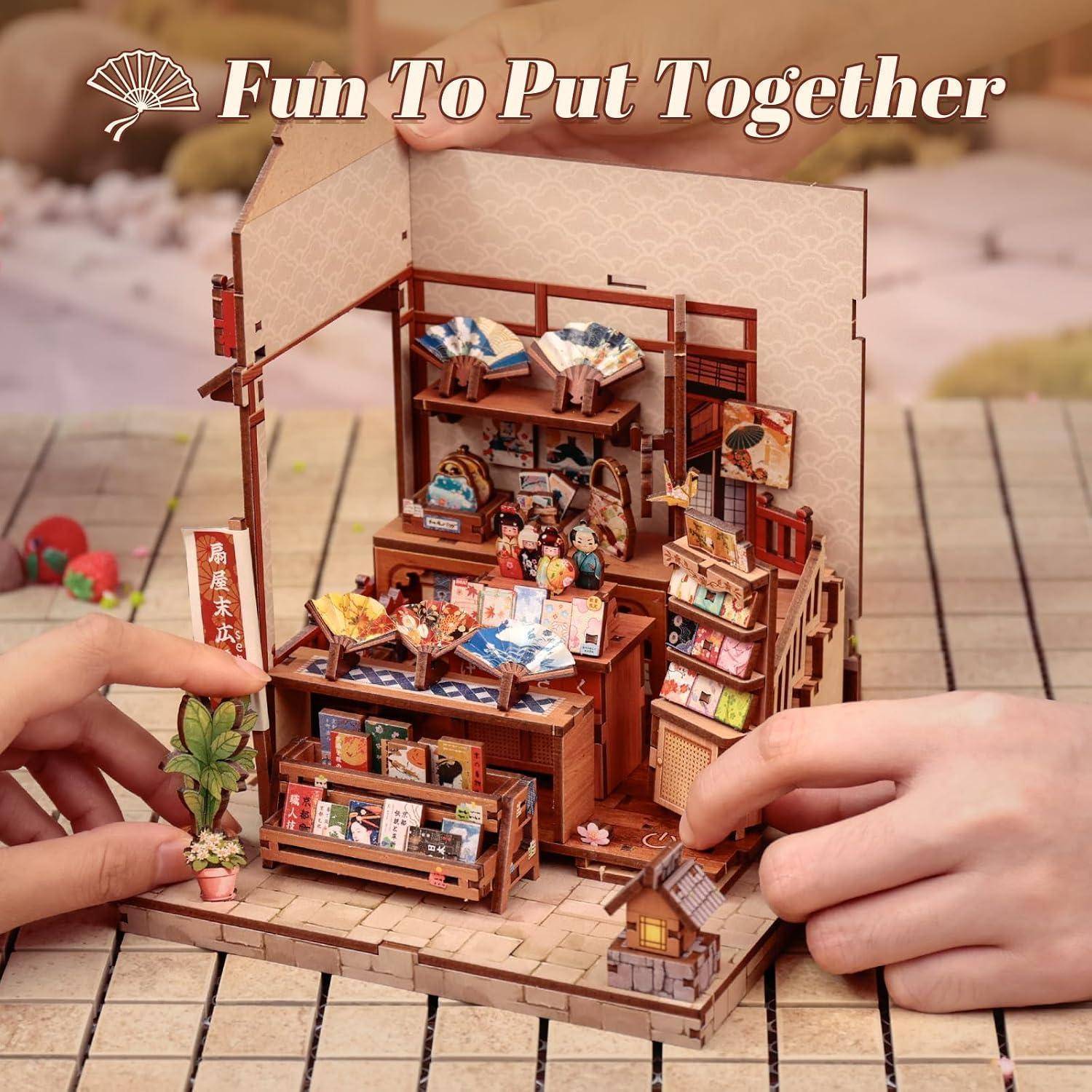 Hände, die ein Miniatur-Buchladen-/Café-Diorama-Set mit der Aufschrift „Macht Spaß zum Zusammenbauen