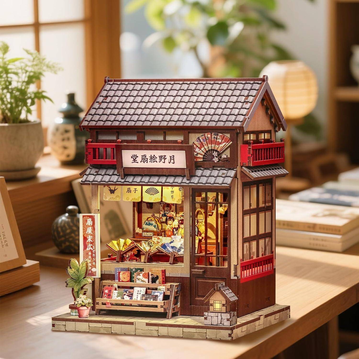 Ein detailliertes Miniatur-Modell eines japanischen Geschäfts auf einem Holztisch, mit beleuchteten Schaufenstern, roten Balkonen und einem Schild mit japanischen Schriftzeichen.