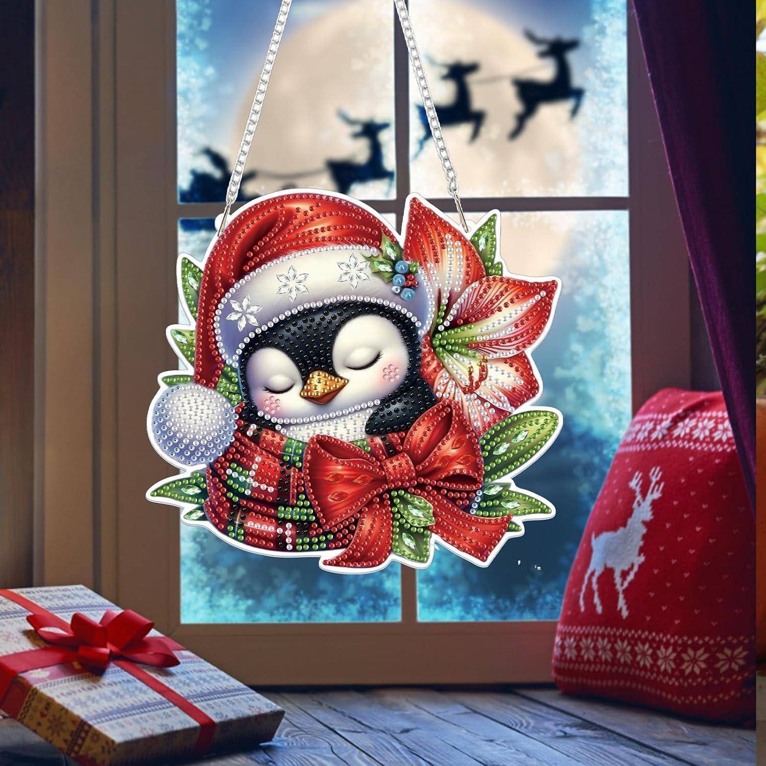 Dekorativer Pinguin-Weihnachtsschmuck mit rotem Schal und Schleife, der vor einem Fenster hängt; Geschenkbox und roter Winterpullover in der Nähe.