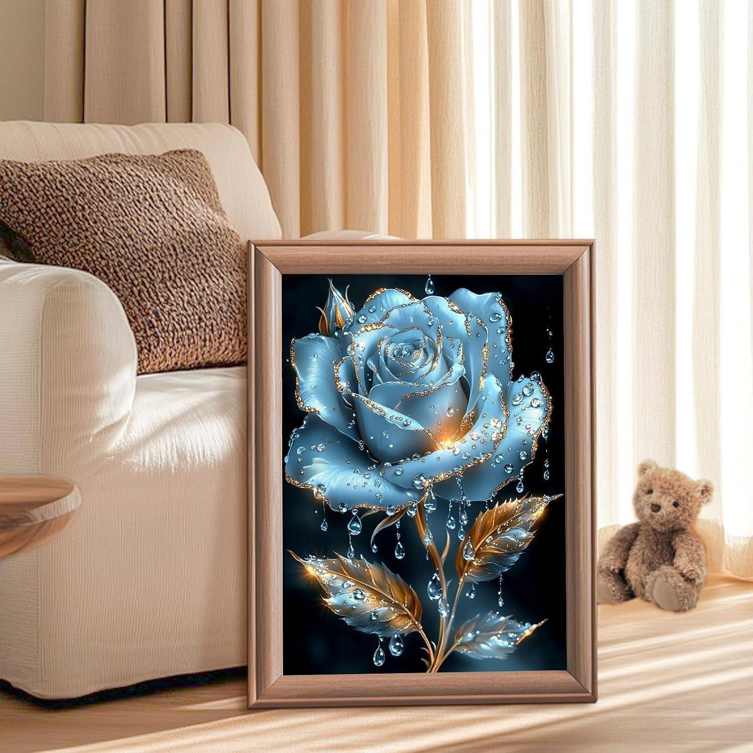 Gerahmtes Kunstwerk einer blauen Rose mit goldenen Blättern und Wassertropfen, das auf dem Boden in einem gemütlichen Wohnzimmer neben einem Stuhl und einem Teddybären ausgestellt ist.