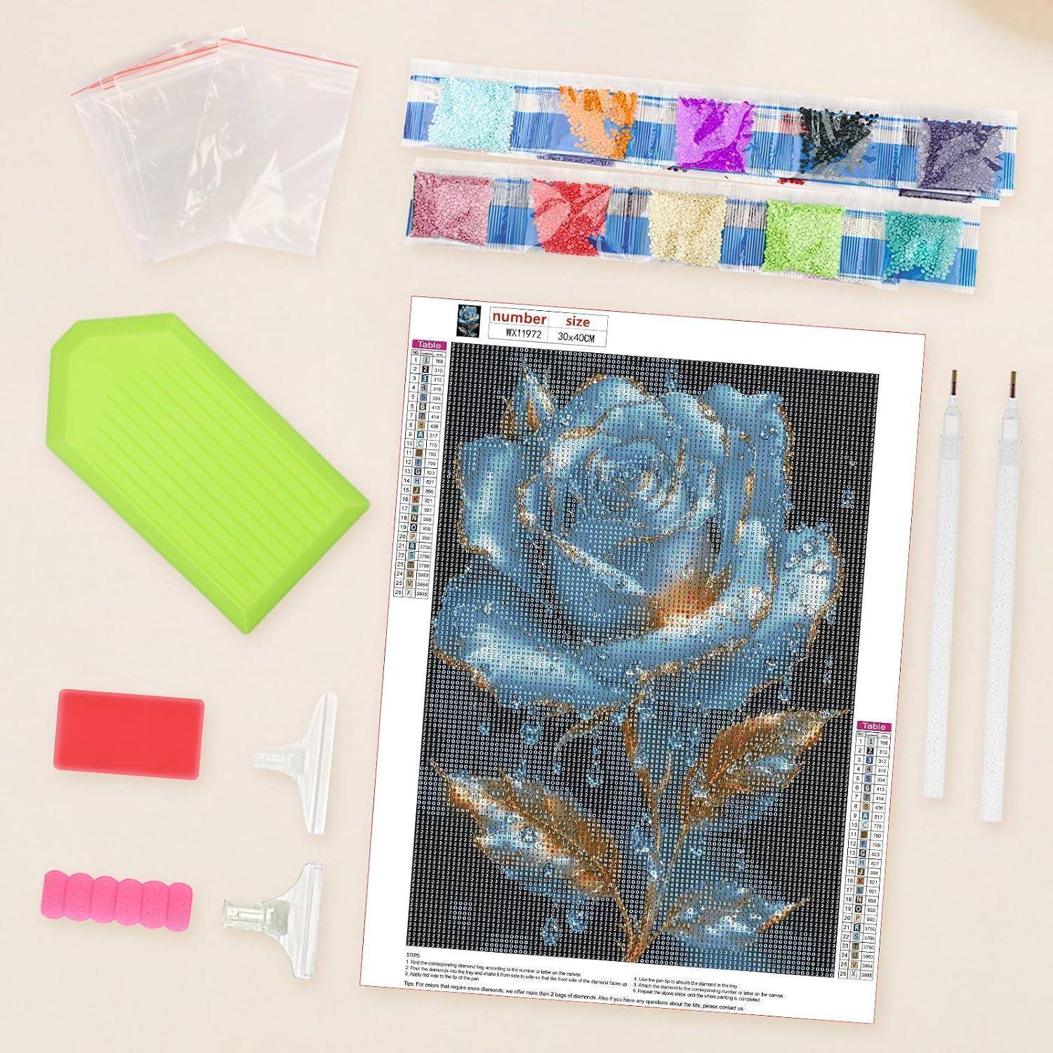 Diamantmalerei-Set mit blauem Rosenmuster, Schmucksteinstreifen, Applikationsstiften, Tablett, Wachs und Aufbewahrungstaschen auf einem Tisch.