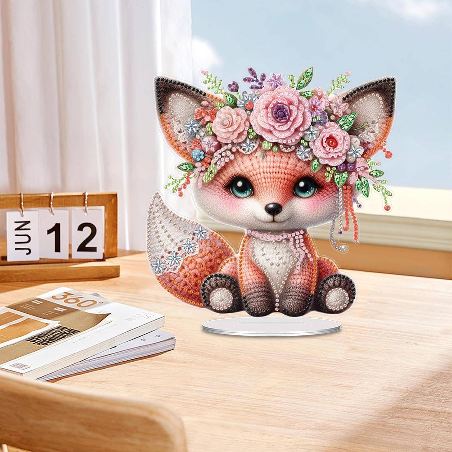 Dekorative Fuchsfigur mit Blütenkrone auf einem Schreibtischkalender, der den 12. Juni zeigt, neben Zeitschriften auf einem Holztisch.