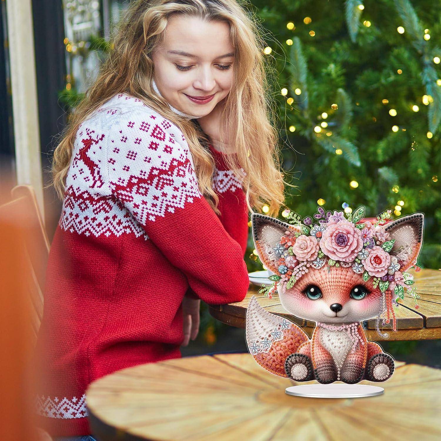 Eine Frau in einem roten Winterpullover schaut sich eine kleine dekorative Fuchsfigur mit Blumen auf einem Tisch im Freien an.