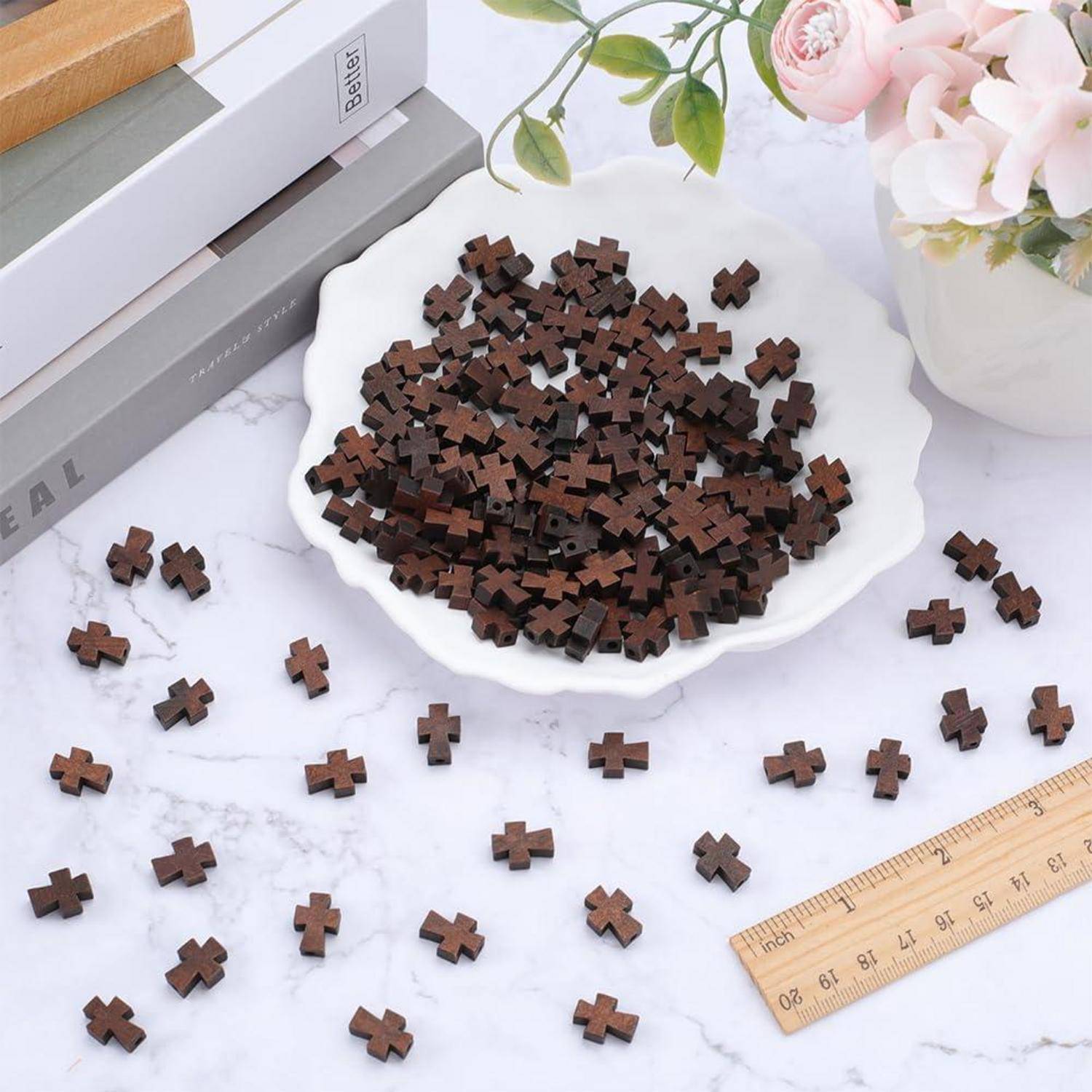 Haufen von kleinen dunklen hölzernen kreuzförmigen Teilen in einer weißen Schüssel, mit verstreuten Teilen, Büchern, Blumen und einem Lineal auf einer Marmoroberfläche.