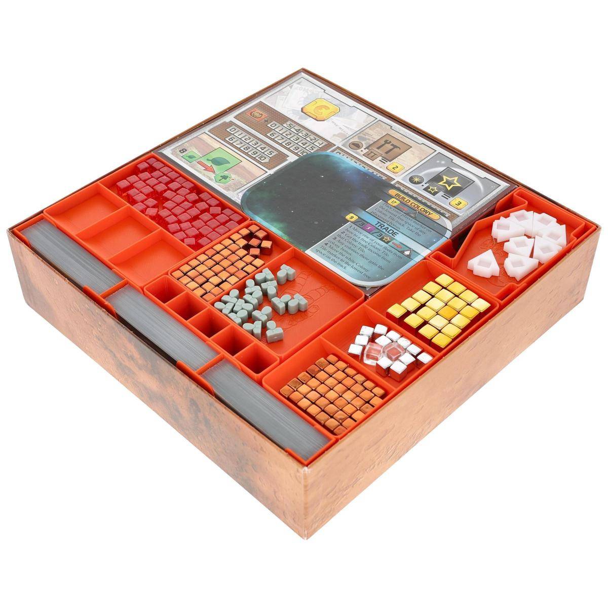 Offene Brettspielschachtel mit orangefarbigen Kunststoff-Organisationsschalen, die farbige Spielsteine, Würfel und Karten in Fächern angeordnet halten.