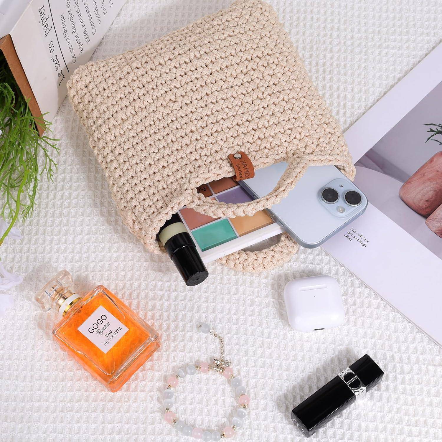 Eine gewebte beigefarbene Handtasche mit einem Telefon, Makeup-Palette, Lippenstift, Parfüm, Ohrhörer-Etui und Lippenstift auf einer weißen strukturierten Oberfläche arrangiert.