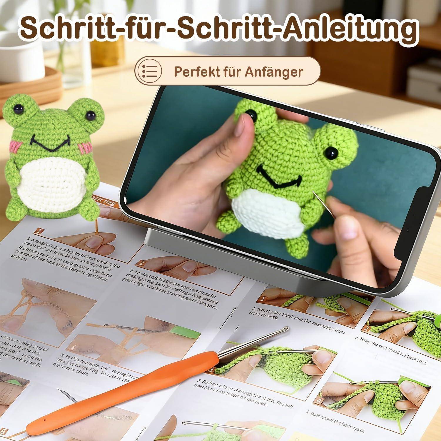 Deutsch-Anleitungs-Bild, das eine anfängerfreundliche Schritt-für-Schritt-Anleitung zum Häkeln eines kleinen grünen Frosch-Plüschs zeigt, mit gedruckten Anweisungen und einem Telefon, das den Prozess demonstriert.