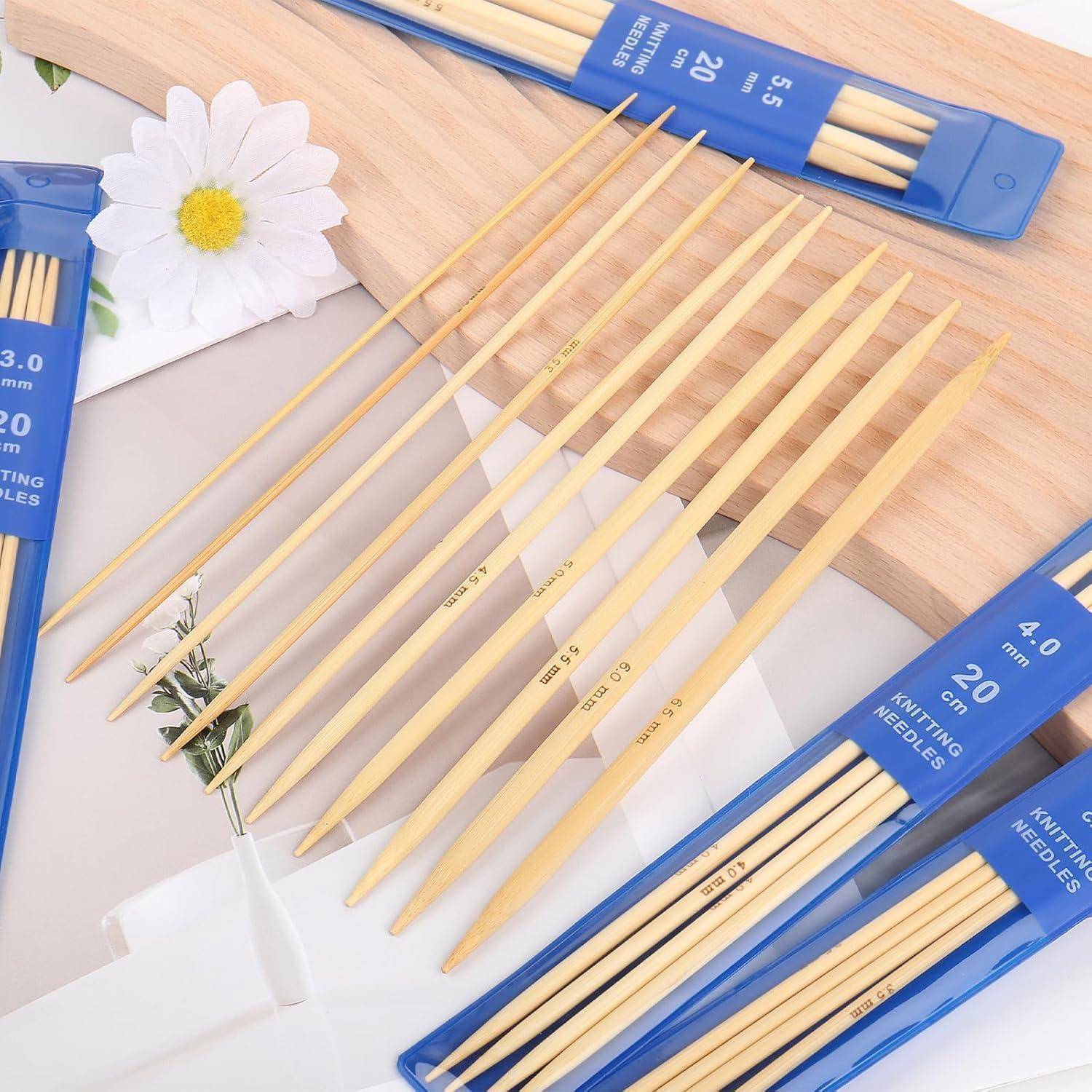 Satz aus Bambus-Stricknadeln in blauen Kunststoffhülsen, diagonal auf einer hellen Holzoberfläche angeordnet, mit einer weißen Blume in der Nähe.