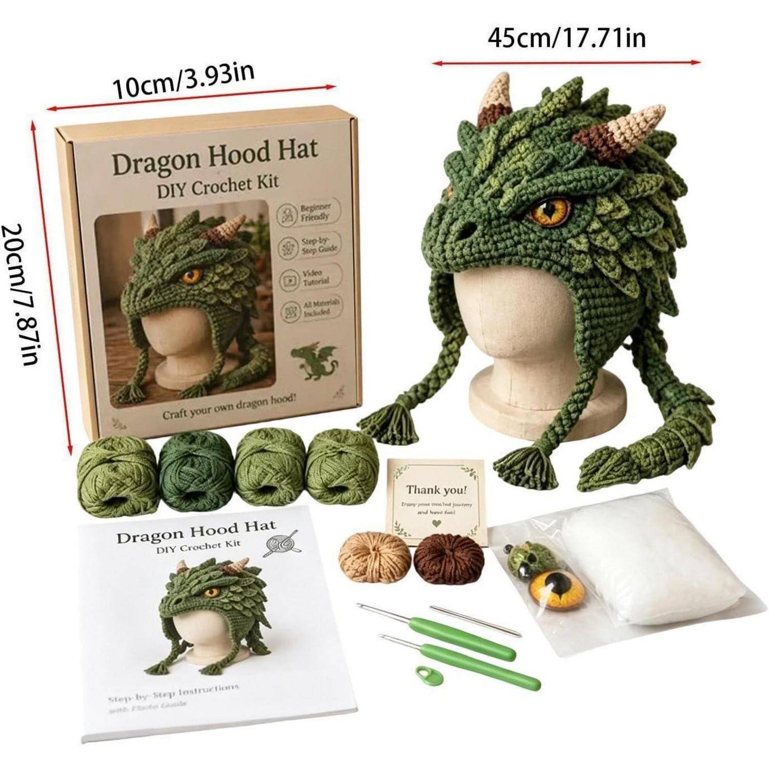 Häkelset für Drachenhaube mit grüner Drachenmütze auf einem Mannequinkopf ausgestellt, plus Garn, Werkzeuge, Musterheft und Verpackung mit Abmessungen.