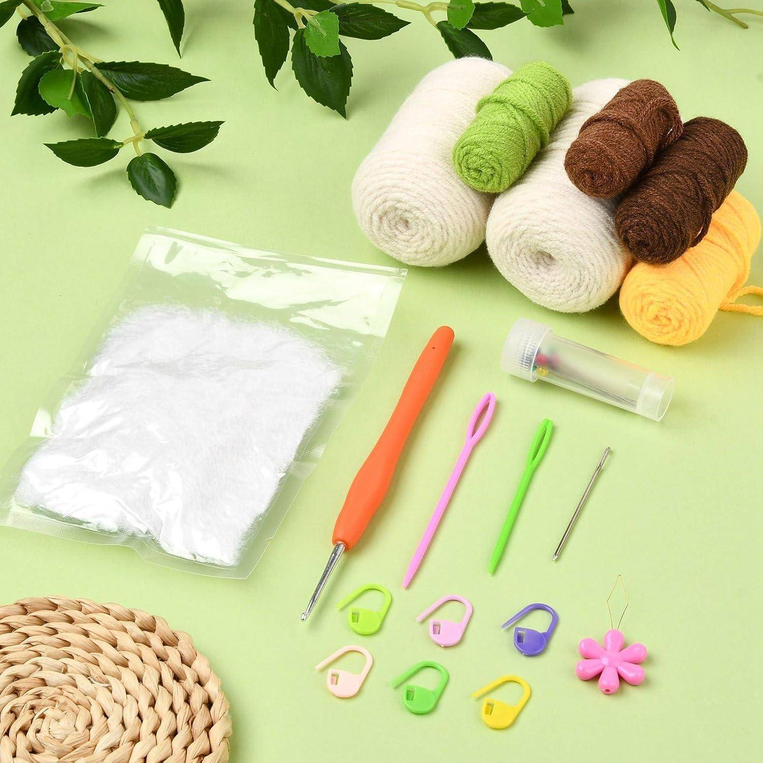 Strickzubehör auf einer grünen Oberfläche: Wollknäuel, Häkelnadel, Stricknadeln, Maschenmarkierer, weiße Füllwolle und eine Kante aus gewebter Matte.