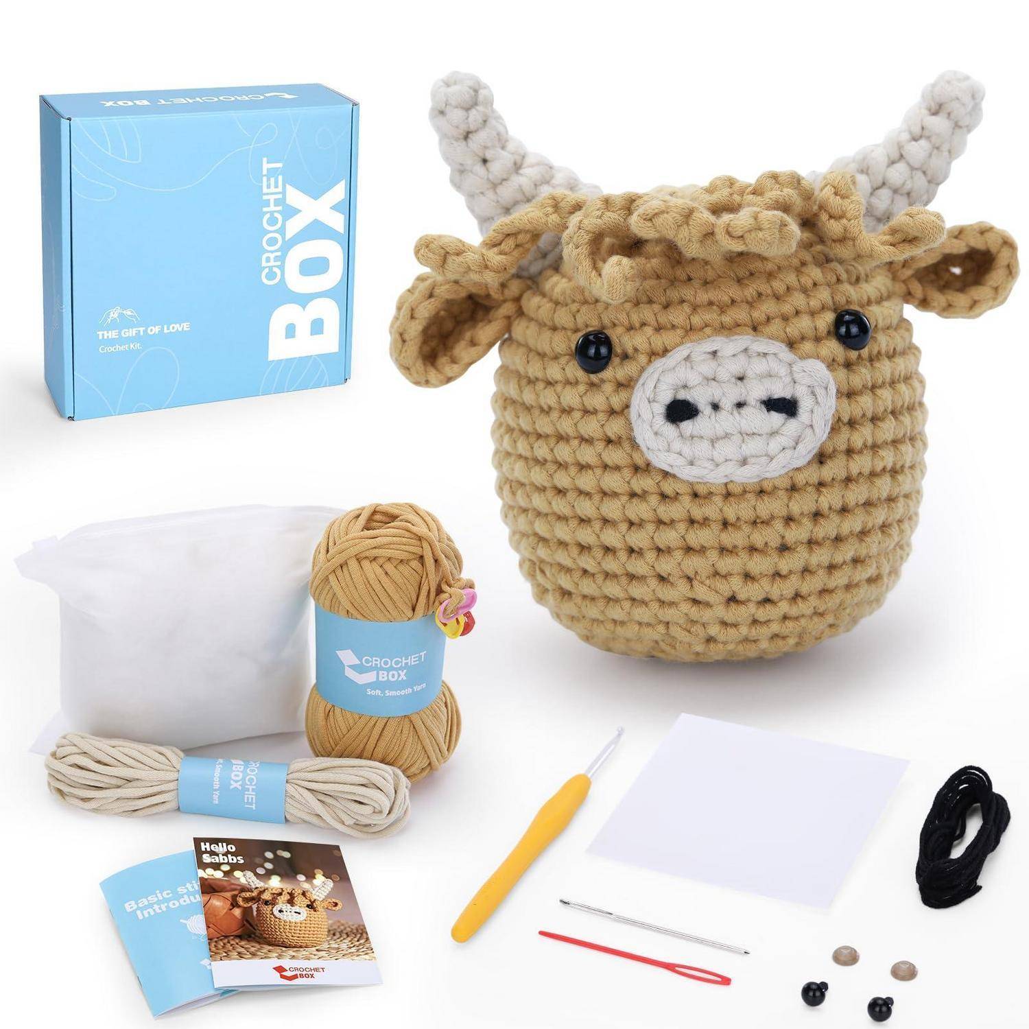 Häkelkasten-Set mit Garn, Häkelhaken, Nadeln, Füllmaterial und Anleitungen, gezeigt neben einem gehäkelten Stierkopf mit Hörnern und Ohren.