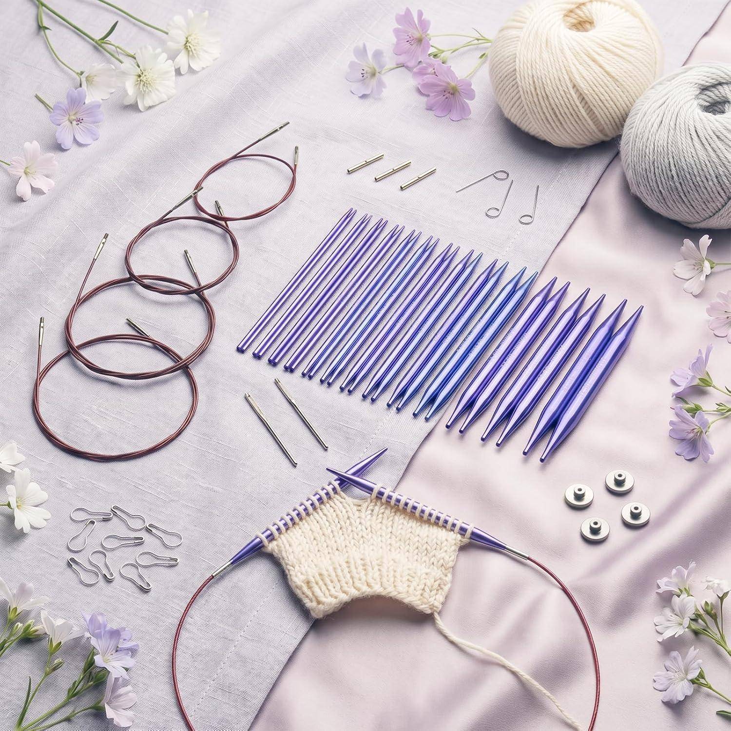 Strickzubehör auf einem Stoff ausgebreitet: Rundstricknadeln, austauschbare Nadeln, Verbindungskabel, Maschenmarkierer, Wollknäuel und ein kleines cremefarbenes Muster in Arbeit.