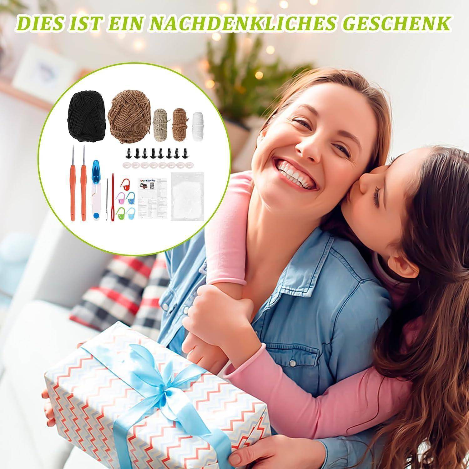 Lächelnde Frau umarmt ein Kind, während sie ein verpacktes Geschenk hält; die Einfügung zeigt Häkelbedarf und deutschen Text „DIES IST EIN NACHDENKLICHES GESCHENK