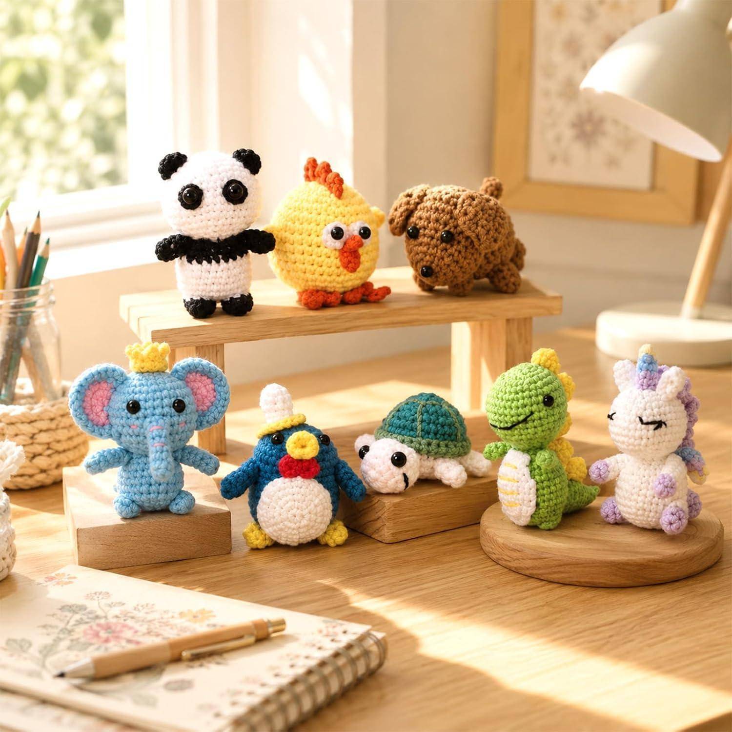 Kleine gehäkelte Tierfiguren auf Holzständern auf einem sonnigen Schreibtisch ausgestellt, darunter ein Panda, ein Küken, ein Hund, ein Elefant, ein Pinguin, eine Schildkröte, ein Dinosaurier und ein Einhorn.