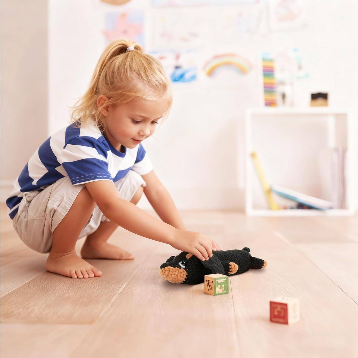 Ein kleines Kind hockt auf dem Boden und spielt mit einem Kuscheltier und Holzbauklötzen in einem hellen Zimmer.