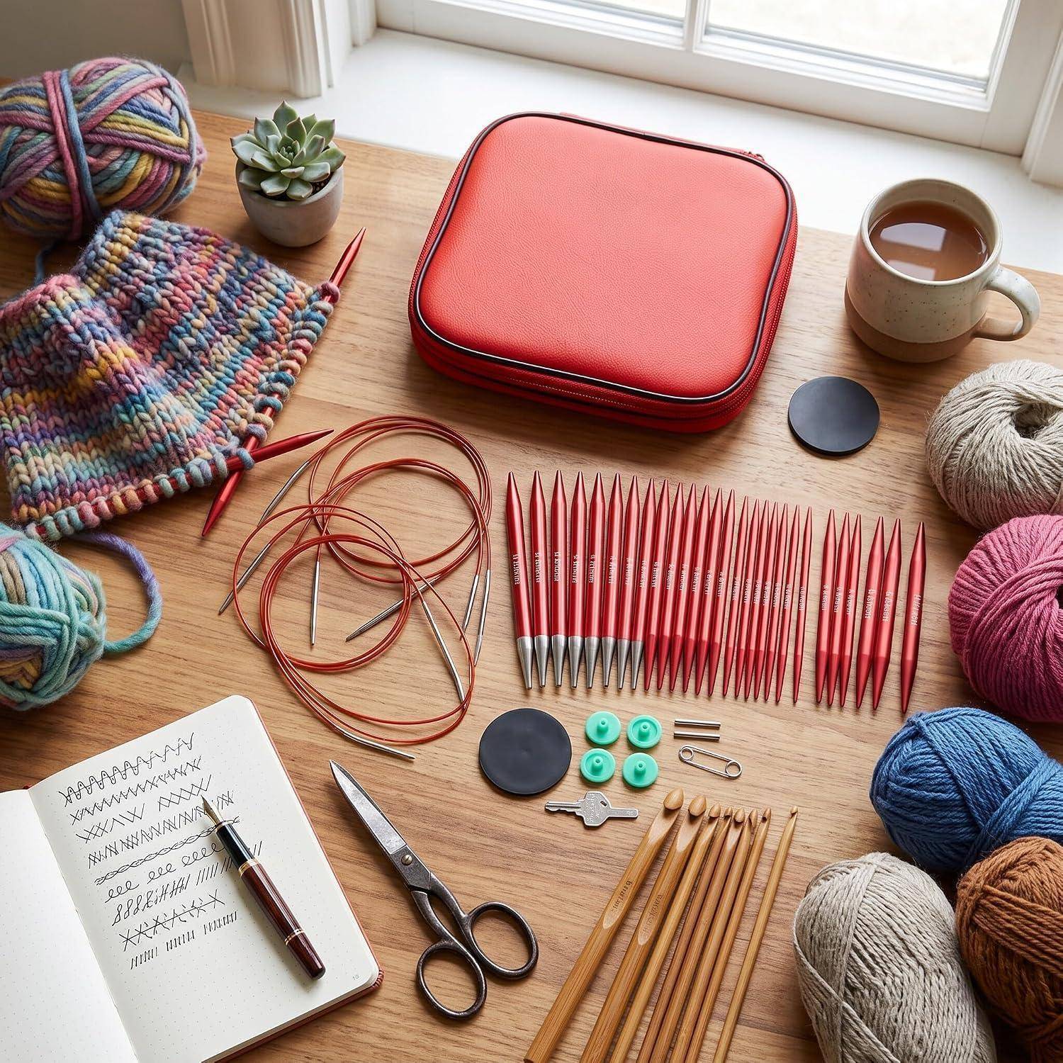 Strickzubehör auf einem Tisch angeordnet: Rundnadeln und Stricknadeln, Wollknäuel, Schere, Notizbuch, Tasse, ein rotes Etui und ein Strickmuster.