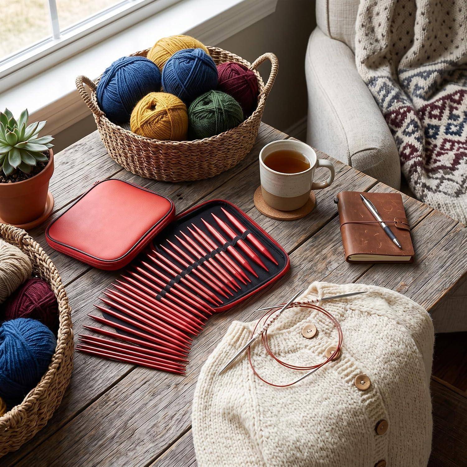 Stricksachen auf einem rustikalen Tisch: Wollkörbe, rote Stricknadeln in einem Etui, ein Notizbuch, Tee und ein beigefarbenes Strickkleidungsstück in Arbeit.