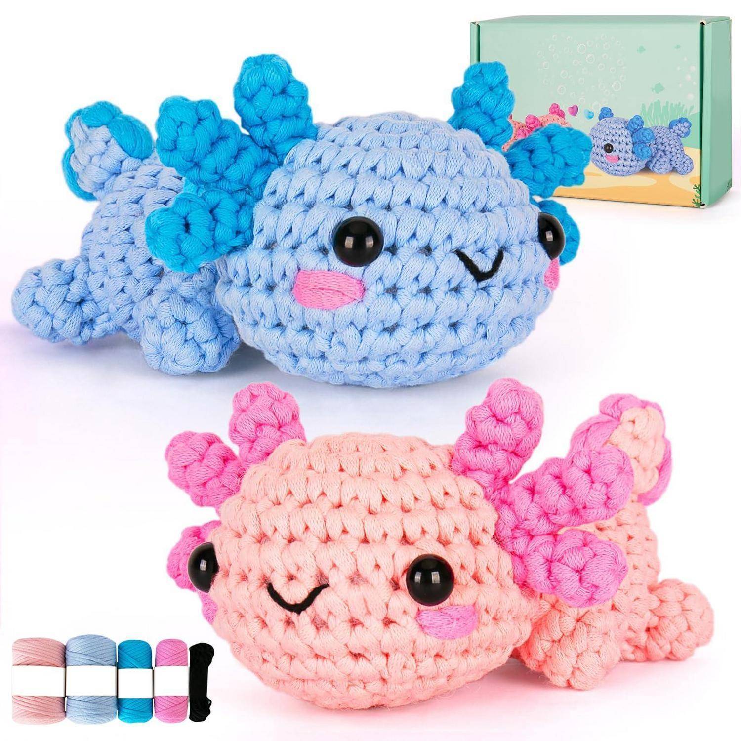Zwei gehäkelte plüschige Axolotl-Spielzeuge, eines blau und eines rosa, gezeigt mit einer kleinen Produktschachtel im Hintergrund.